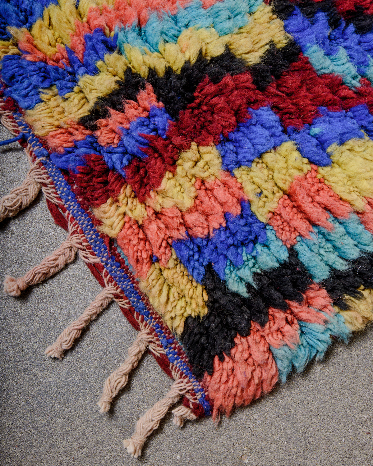Corner of Berber runner rug with brightly coloured wool pile and natural wool tassels.